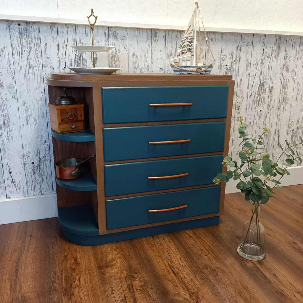 Holzkommode mit 4 Schubladen in blau und Kupfergriffen, links 3 Regale, von vorn mit Deko